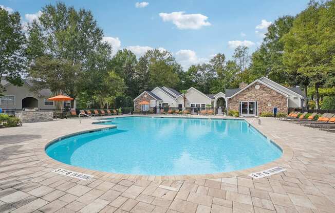 A large outdoor swimming pool surrounded by a brick patio and lounge chairs.