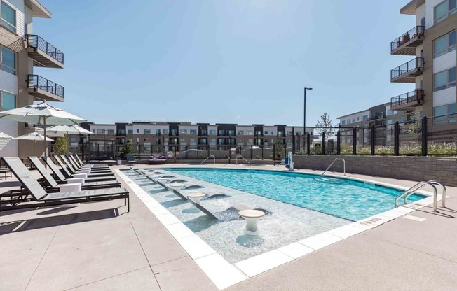 a pool with lounge chairs and an apartment building in the background