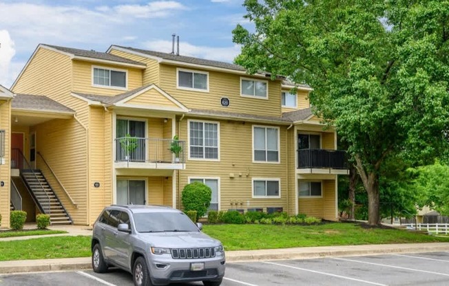 A silver SUV is parked in a parking lot in front of a yellow apartment building.