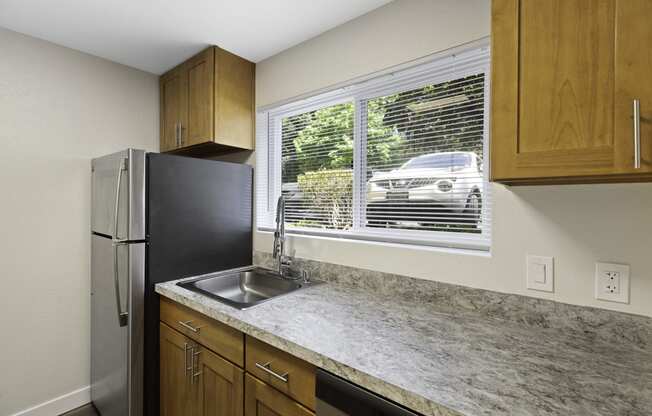 Spacious Kitchen with Wooden Cabinetry, Refrigerator, and Wide Windows Looking in Front Space at Park 210 Apartment Homes, Edmonds, WA, 98026