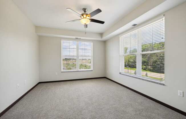 an empty living room with three windows and a ceiling fan