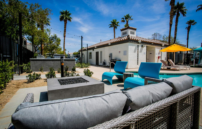 a patio with blue chairs and a fire pit in front of a white house