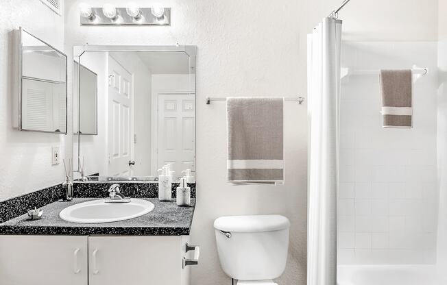 Virtually staged bathroom with large mirror, gray countertop, medicine cabinet, white cabinets and tiled tub with white shower curtain