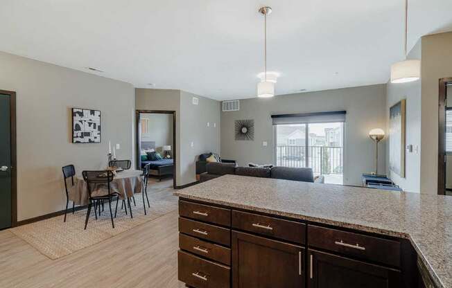 A kitchen with dark wood cabinets and a granite countertop in front of a living room