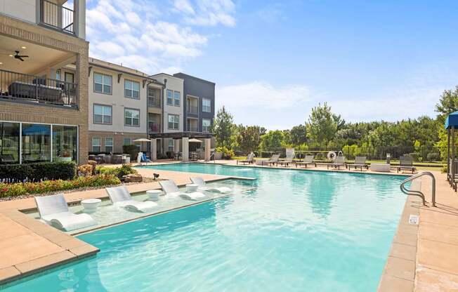 A large swimming pool with lounge chairs and apartment buildings in the background.