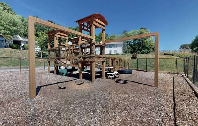 a large playset with a large wooden structure in the middle of a gravel area