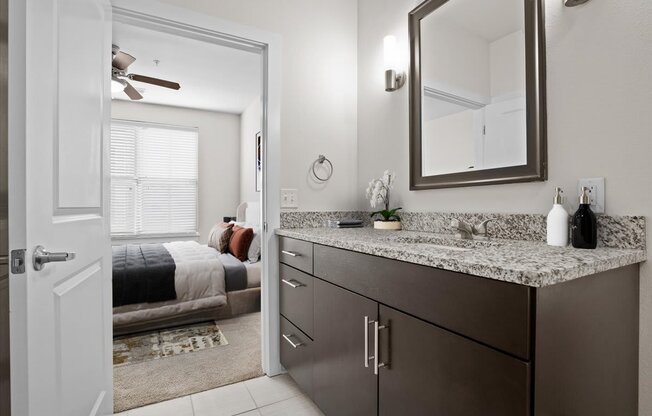 a bathroom with a sink and a mirror and a bedroom