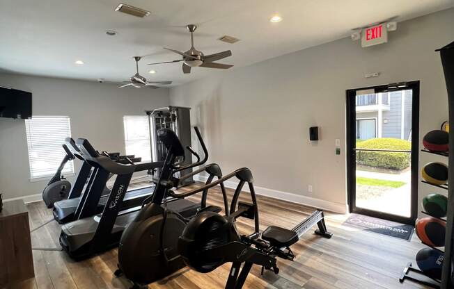 a gym with cardio equipment and a door leading to a yard