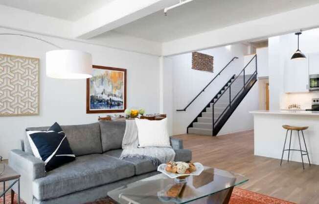 A grey couch with a white pillow and a glass table in front of it.