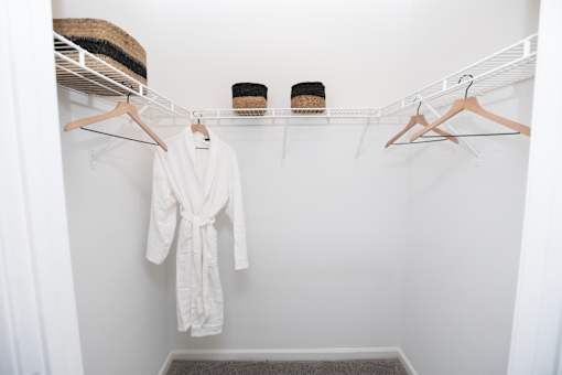 A white robe is hanging on a hanger in a white closet.