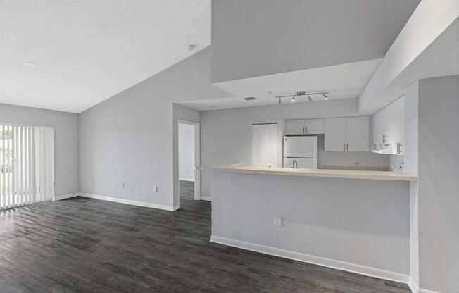 the living room and kitchen of an apartment with white walls and wood floors