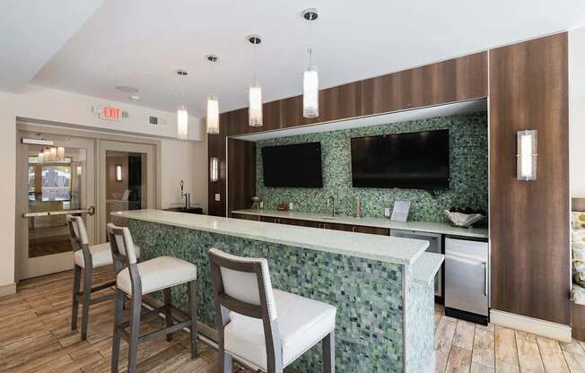 A kitchen with a green backsplash and a bar area with two chairs.
