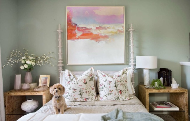 a dog sits on a bed in a bedroom with a painting on the wall
