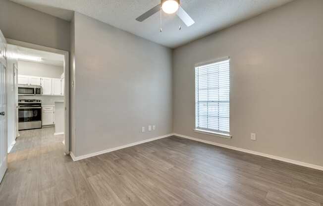 an empty living room with a ceiling fan and a kitchen