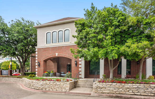 A red brick house with a stone wall and a green tree in front.