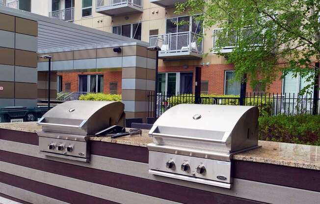 Two silver barbecue grills on a striped concrete surface.