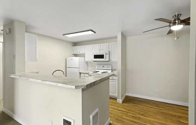 a kitchen with an island, plank flooring, overhead lighting, and a ceiling fan in the dining area at Serra Vista Apartment Homes, Lynnwood, Washington 98087