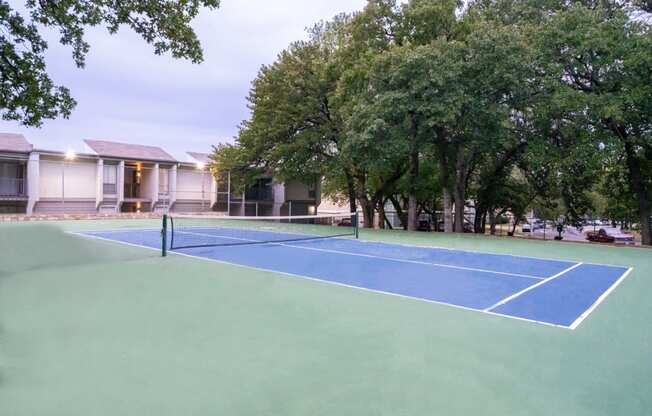 a tennis court with trees and a house in the background