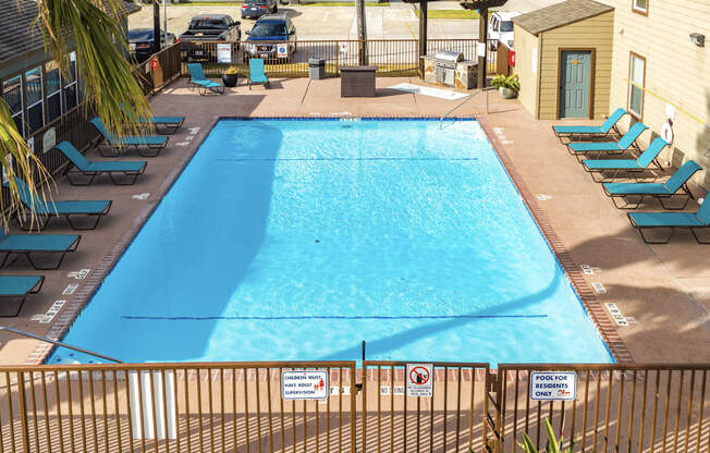 A pool surrounded by chairs and a fence.