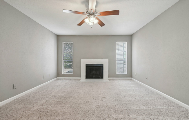 Cozy living room with plush carpet, elegant ceiling fan, and a classic fireplace, offering a serene ambiance at Driscoll Place.