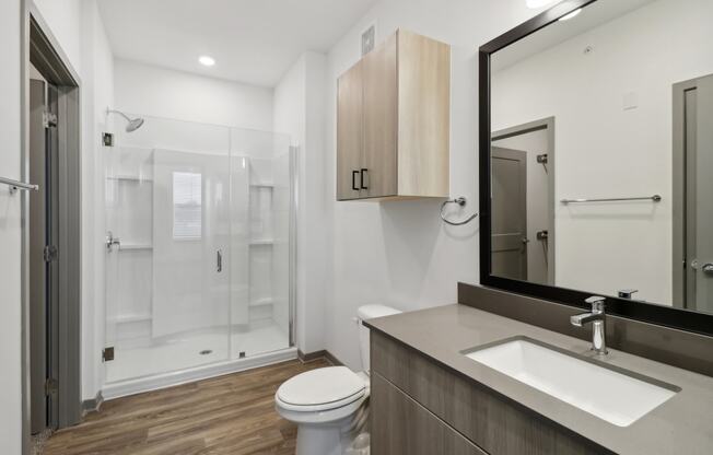 a bathroom with a toilet sink and mirror and a shower at The Depot in The Depot Raymore, MO 64083