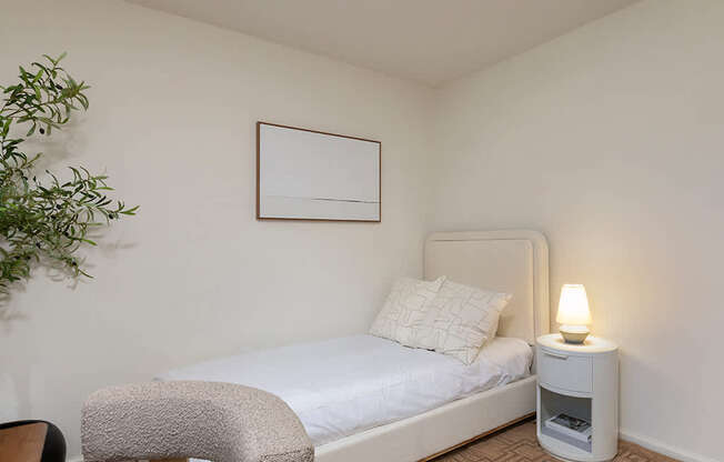 A bedroom with a bed, chair, and a plant.