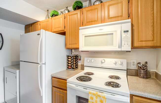 Staged kitchen with white appliances, wood cabinetry, granite style counter tops, and full-size dryer in the background.