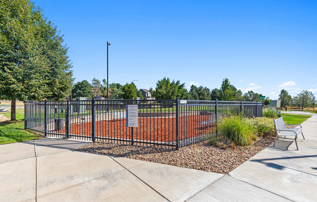 a park with a tennis court and a bench in front of a fence