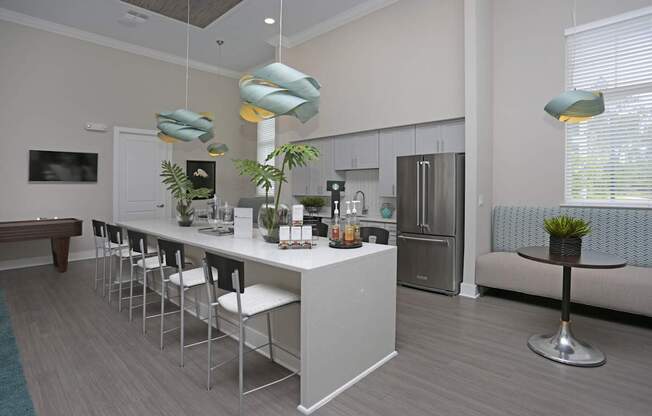 A modern kitchen with a long white island and white chairs.