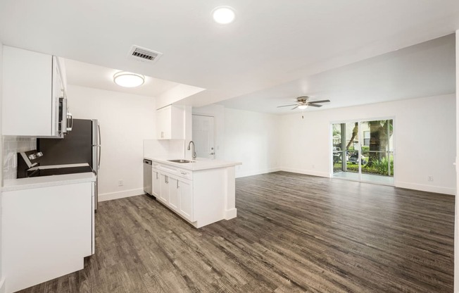 an empty living room with a kitchen and a ceiling fan