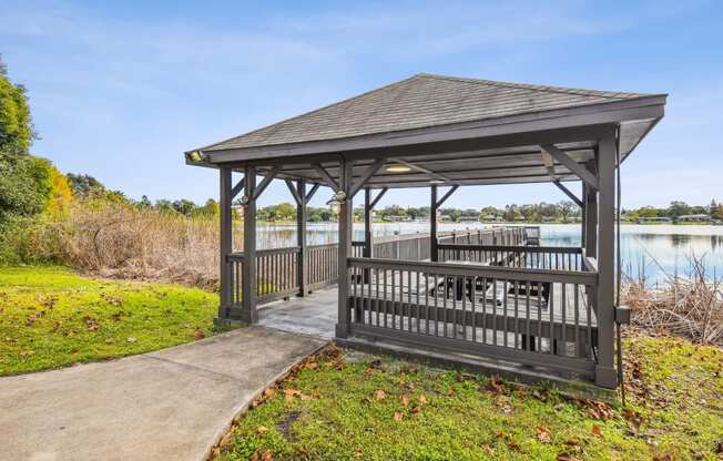 a wooden gazebo with a table and chairs on it next to a lake