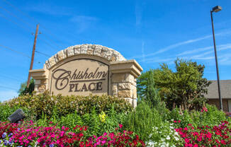 Property signage surrounded by a colorful flower bed at Chisholm Place Apartments in Plano, TX