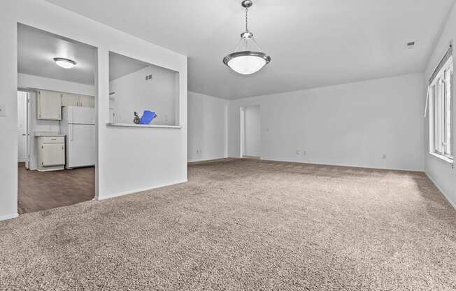 an empty living room with white walls and carpet and a kitchen at Edge At Farmington Hills - Farmington Hills, MI, Michigan