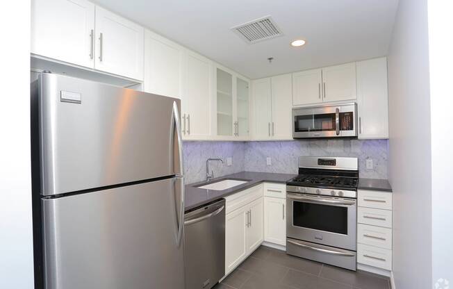 York House kitchen with stainless steel refrigerator, dishwasher, stove and microwave, white cabinets and granite backsplash and countertops. at York House, Saint Louis, Missouri