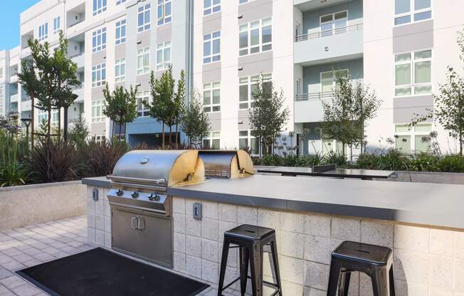 an outdoor kitchen with a grill and stools in front of an apartment building