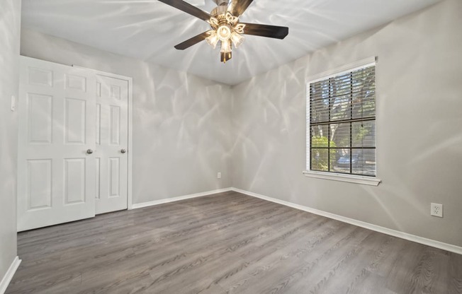 an empty bedroom with a ceiling fan and a window