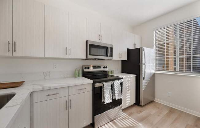 A kitchen with a refrigerator, wooden floors, and white cabinets.