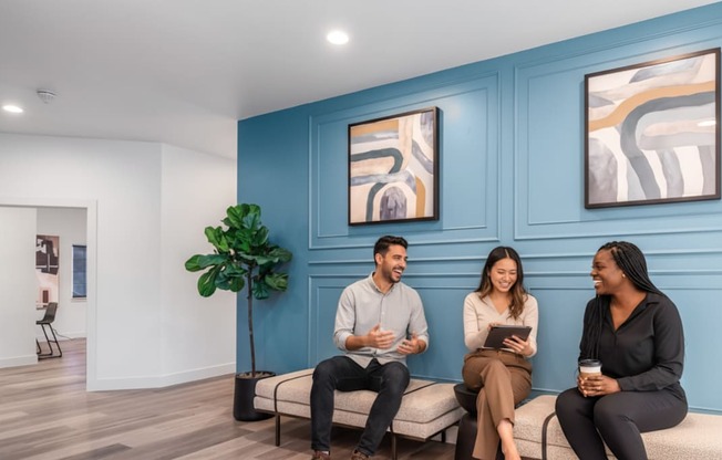 Three people are sitting on a bench in a room with blue walls.