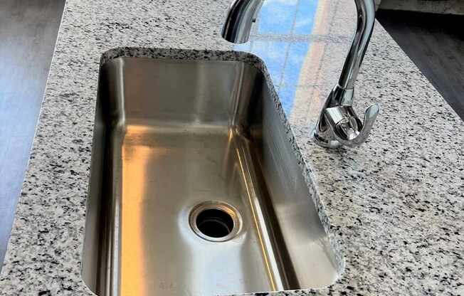 A stainless steel sink with a chrome faucet is installed in a granite countertop.