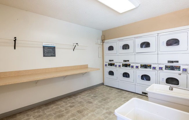 a washer and dryer room in a laundry facility with a row of white at Campbell West Apartments, Campbell, California