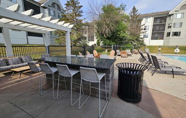 a patio with a table and chairs and a trash can in front of a pool