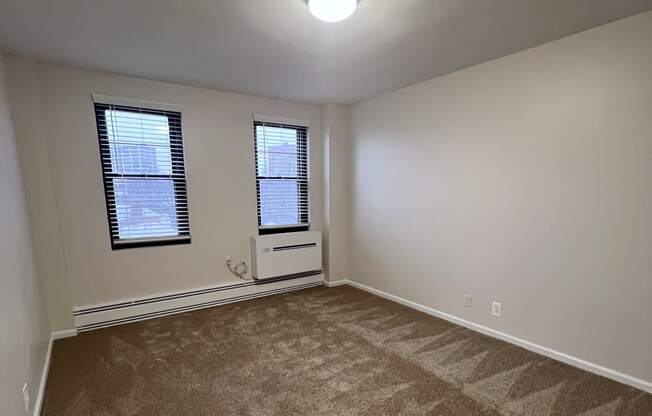 A room with a carpeted floor and a window with blinds.