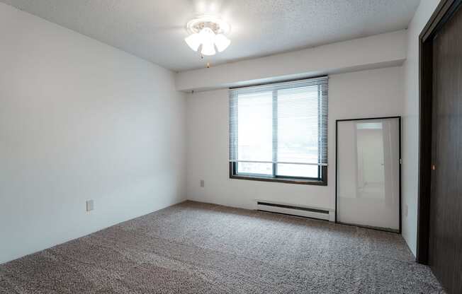 A room with a carpeted floor and a window with blinds. at Bristol Ridge, Urbandale, IA