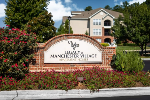 A brick sign that says Legacy at Manchester Village in front of a building.