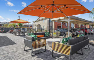 Two chairs and a table are under an orange umbrella.