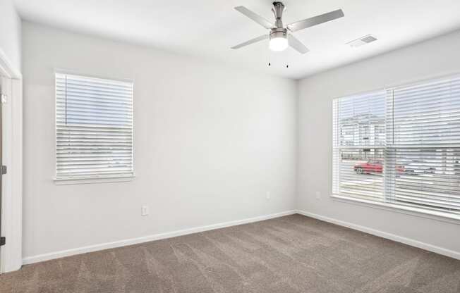 A room with a ceiling fan and two windows with blinds.