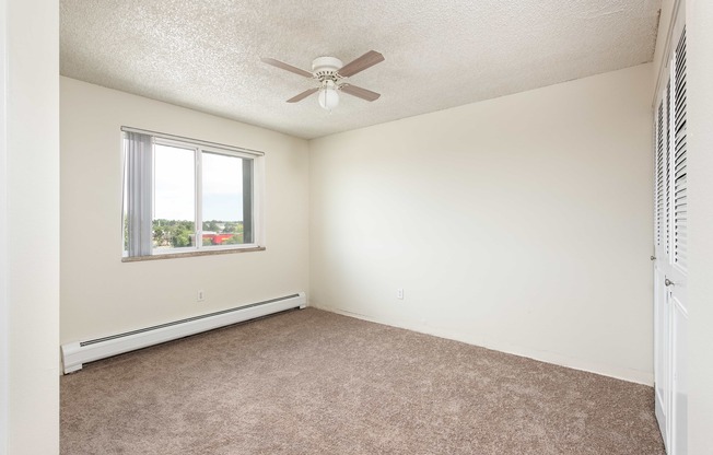 an empty bedroom with a ceiling fan and a window