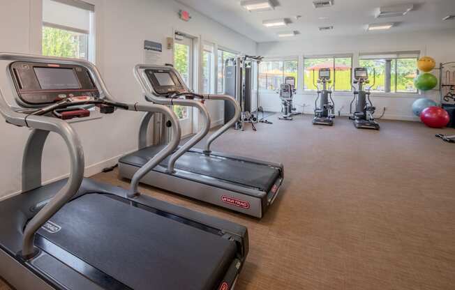 a gym with treadmills and other exercise equipment in a building with windows