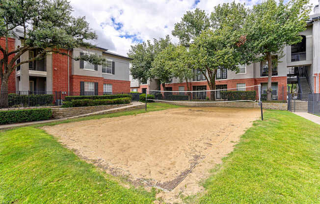 A sand volleyball court is located in the middle of a grassy area.