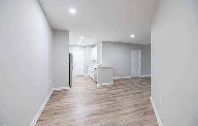 an empty living room and kitchen with white walls and wood flooring